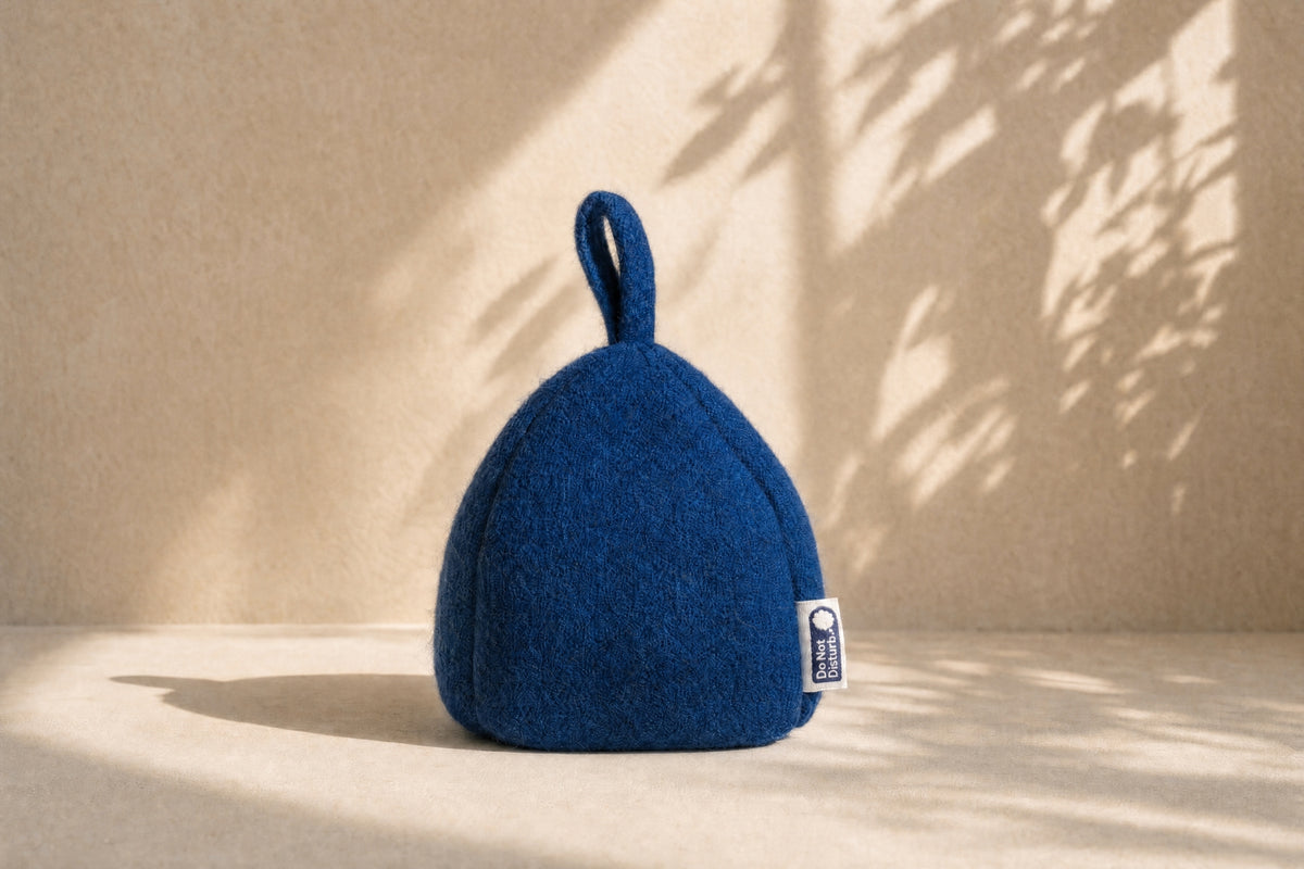 Felted wool door stop in Pacific Blue with its loop handle, standing on a cream floor in warm afternoon light