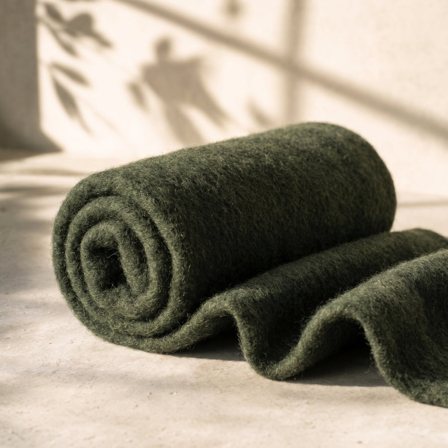 Rolled green felted wool on a light surface with soft shadows