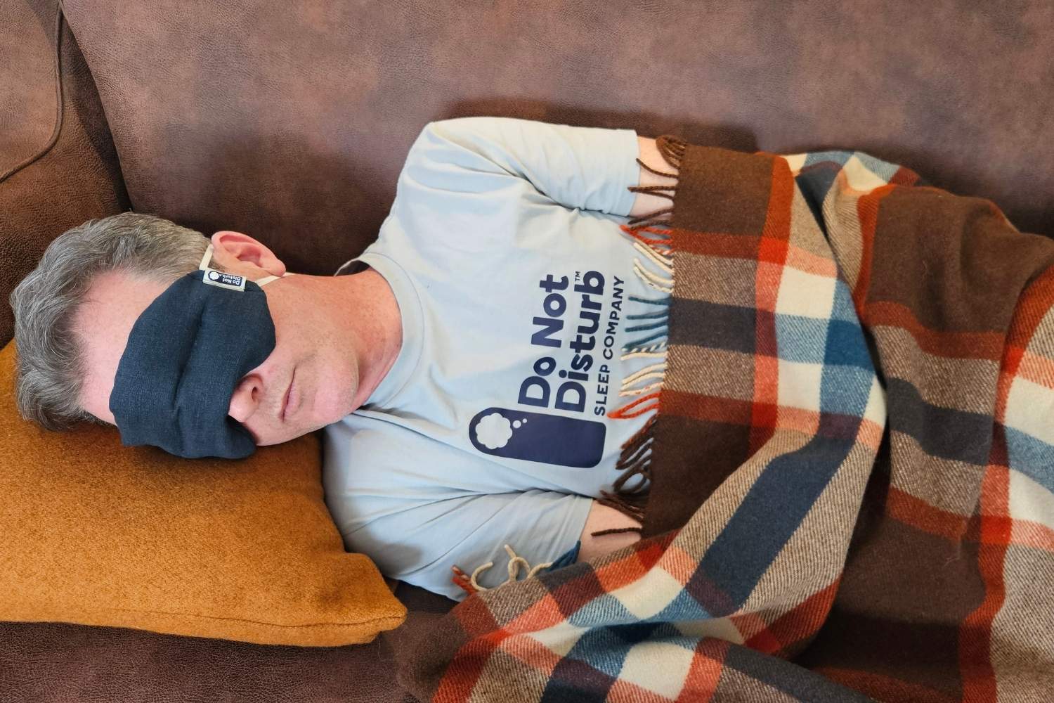 Chris napping on the couch with a Do Not Disturb Weighted Eye Mask