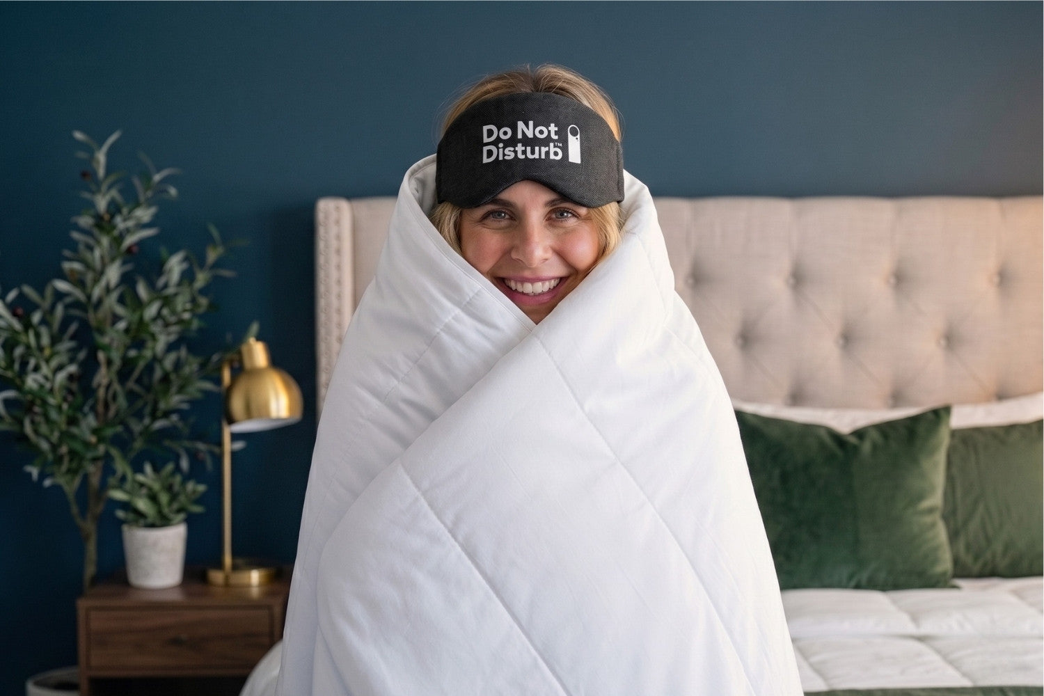 Person wrapped in a blanket with a 'Do Not Disturb' mask on, in a bedroom setting.